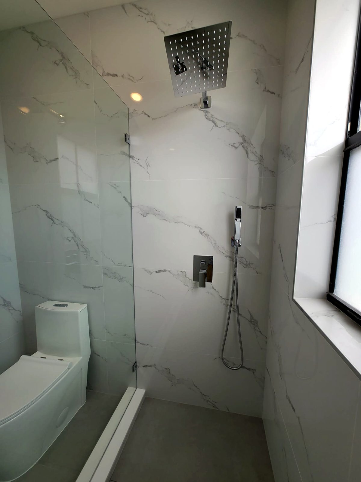 Glass shower with a square rain shower head and marble tile