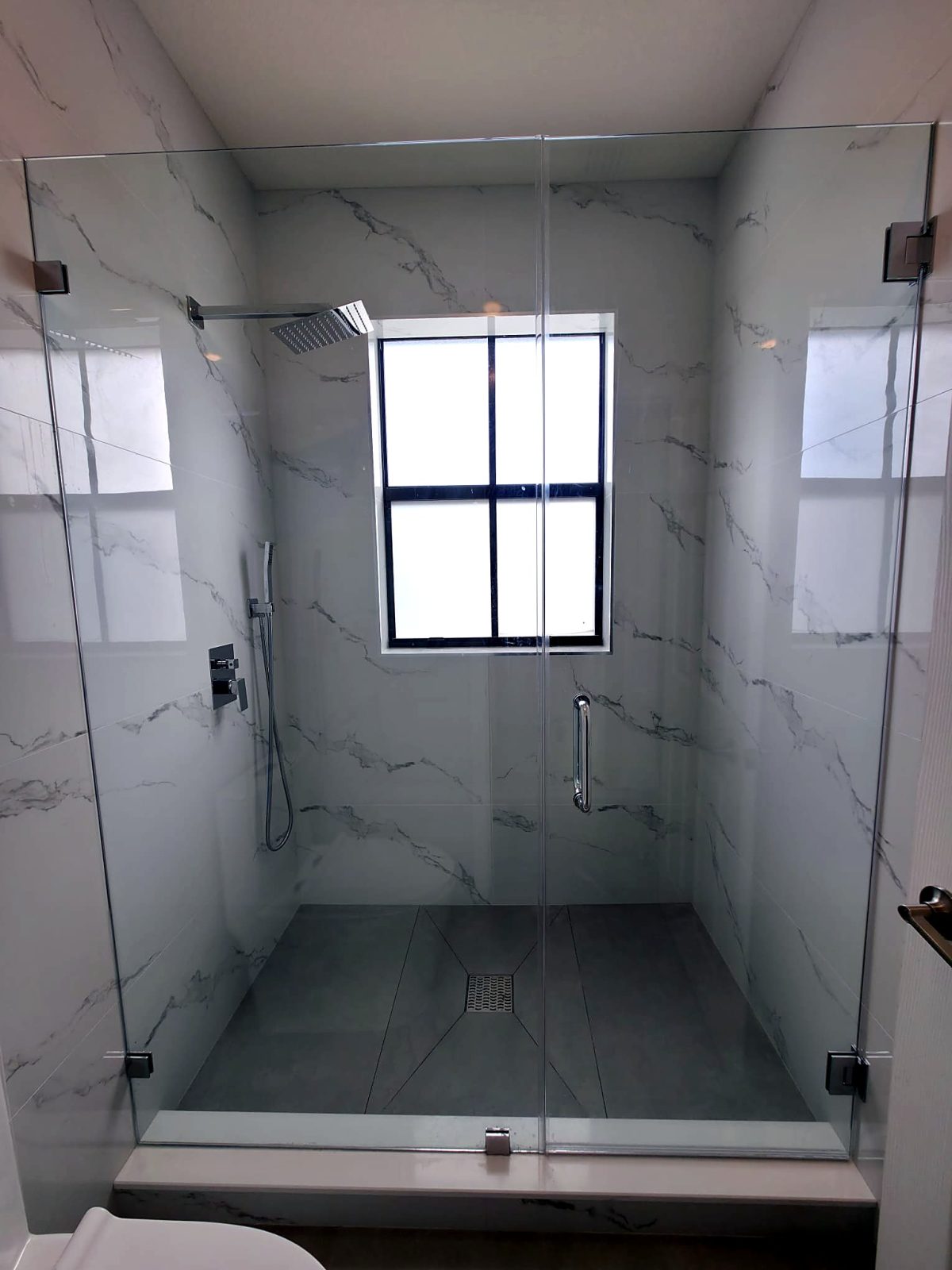Walk-in glass shower with marble tile and a window